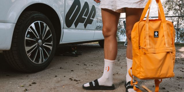 Geheimtipp Camping Italien: eine Person mit Smiley-Socken und orangenem Rucksack steht neben einem weißen Campe rmit der Aufschrift Off.