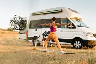 Frau beim Yoga in bunter Kleidung vor ihrem Off Camper