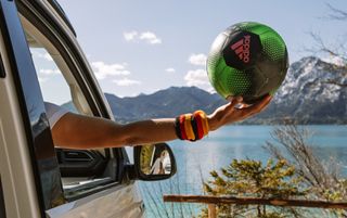 Beim Camping zur Europameisterschaft 2024 hält ein Fan mit Deutschland Schweißband einen grünen Fußball aus dem Fenster seines Campervans am Seeufer