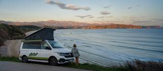 Frau mit Campervan blickt auf Meer