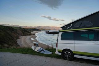 Frau mit Surfboard an der Kueste in Portugal neben Off Camper im Winter